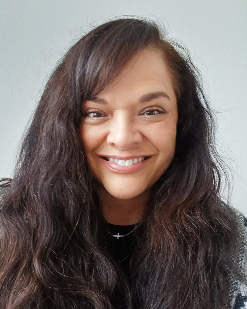 A woman with long brown hair and brown eyes is smiling.