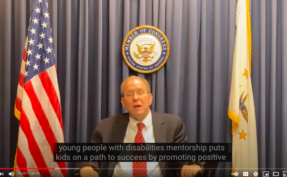 Rep Langevin speaking with flags on either side