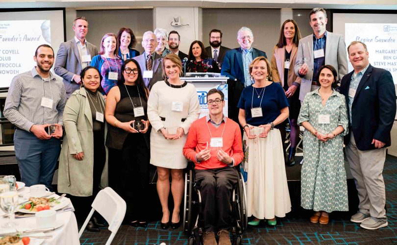 A group of honorees are standing at the Party4PYD stage, holding their awards