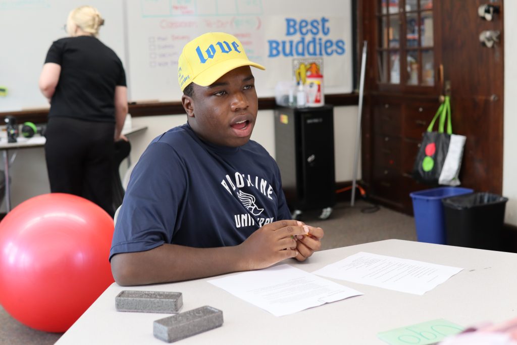A student, wearing a yellow baseball cap, practices answering questions at a mock interview