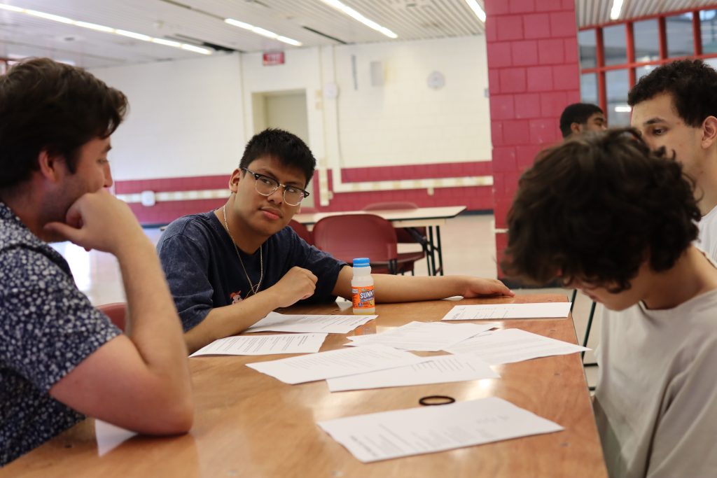 A PYD staff member and students look at job postings, sitting together at a table.