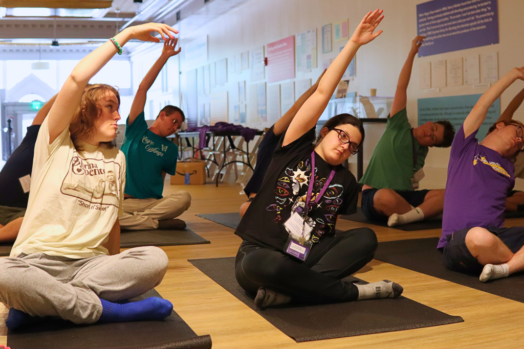 YLF participants stretch their arms up, while sitting on yoga mats.