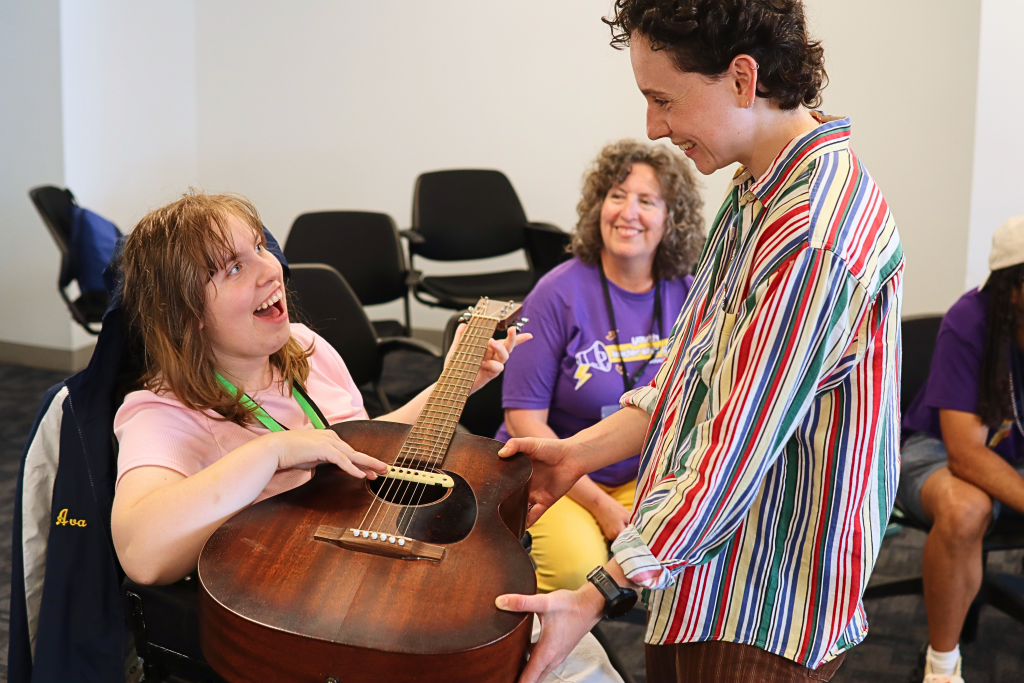 A YLF participant strums an acoustic guitar, smiling up at the workshop instructor.