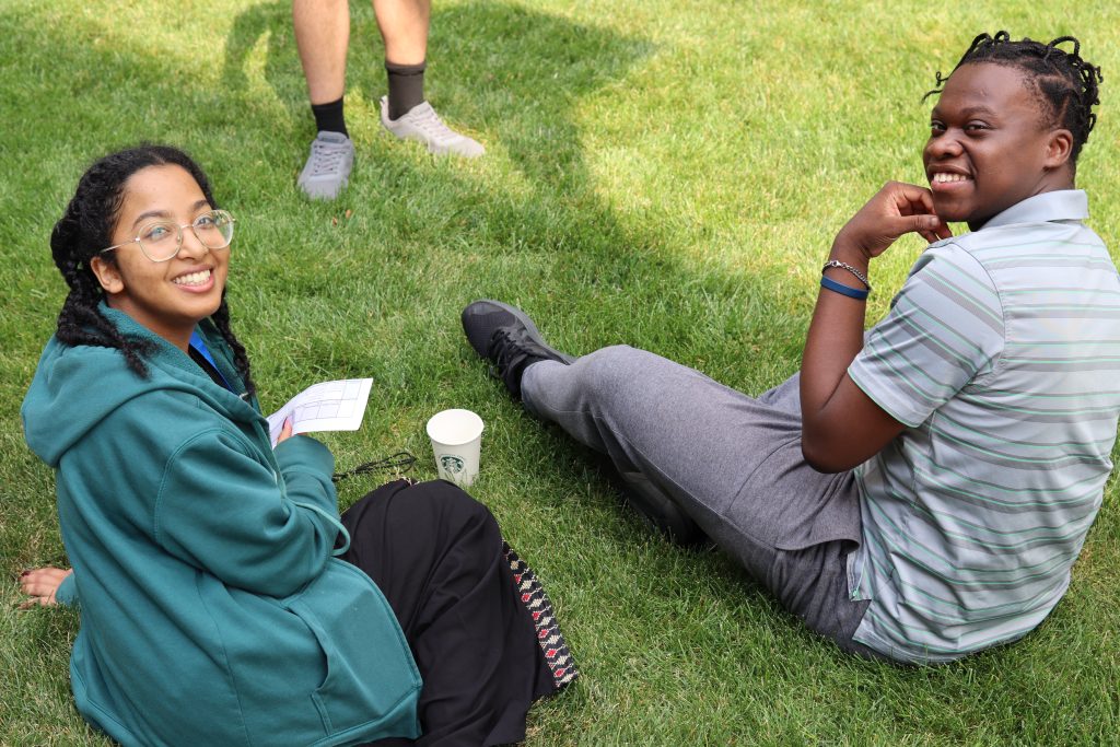 Two participants are sitting on the grass, smiling up at the camera.