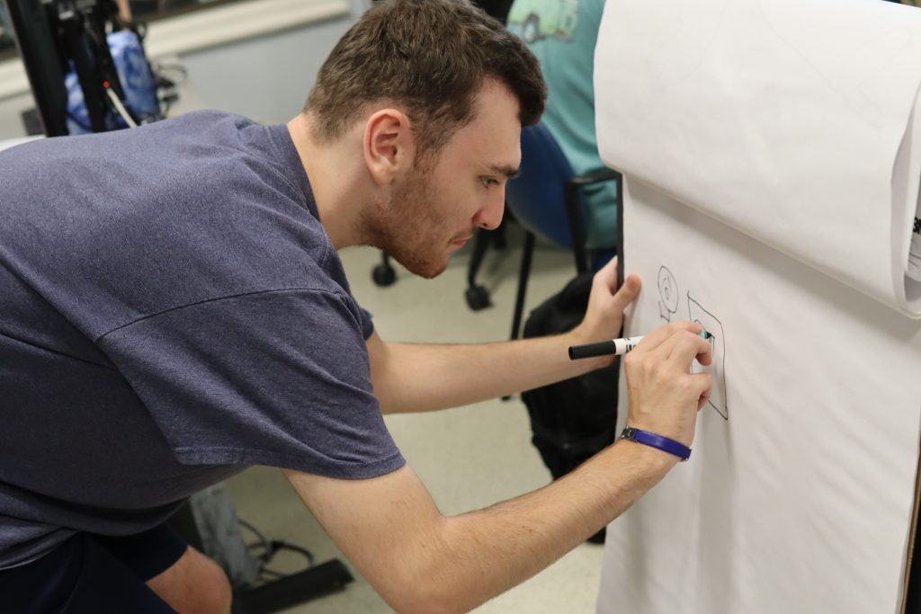 A student leans down to draw on a large piece of paper, during an activity.