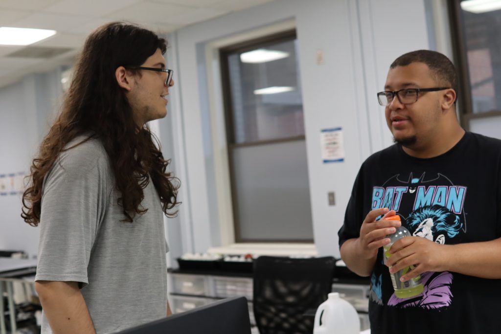 Two students stand next to each other, smiling and talking.